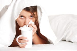 A portrait of a young woman in bed with a cold over white background