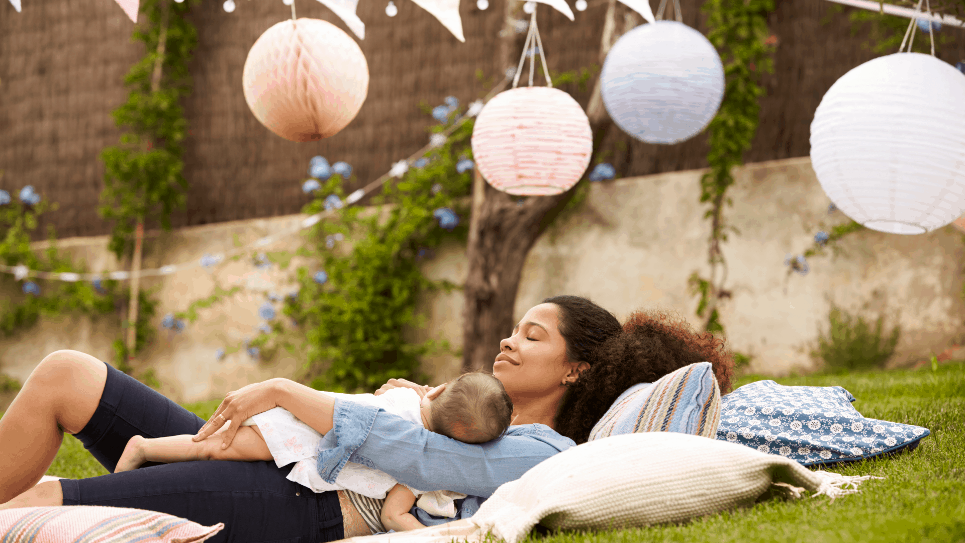 A happy mom lays in the grass on a blanket with her baby. 