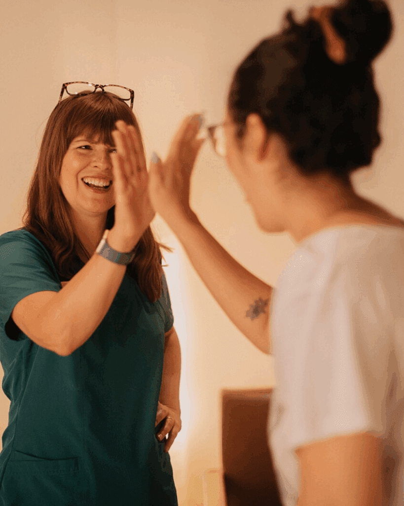 Maegan Hodge, Licensed Acupuncturist at Centered: Richmond Acupuncture, shares a celebratory high-five with a smiling patient in the clinic. Captures patient success and positive treatment outcomes in a warm, welcoming environment.
